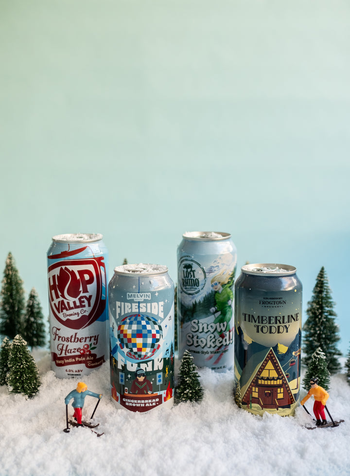 Five beer cans with winter-themed designs on a snowy background with miniature figures and trees.