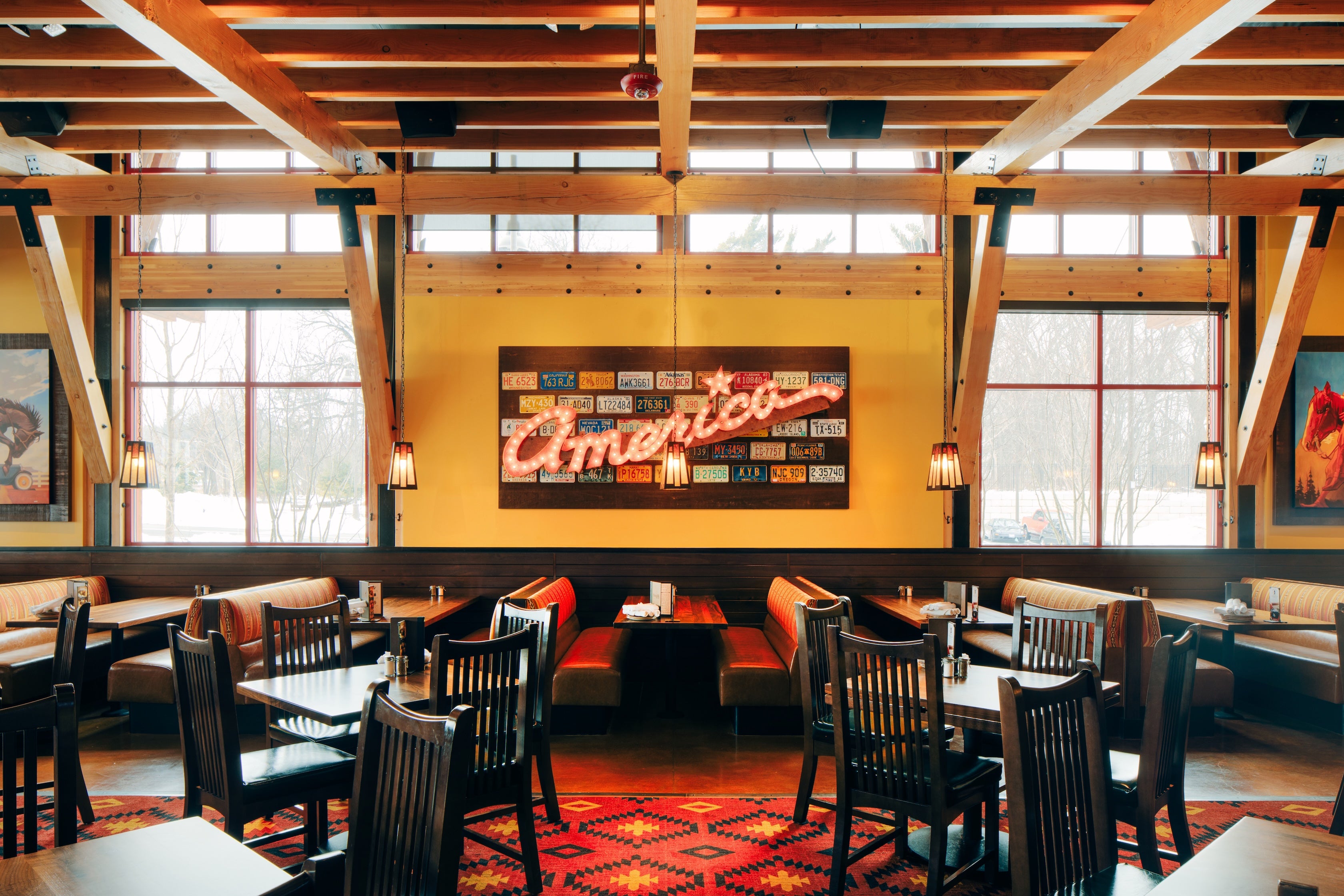 Dining area with wooden beams, tables, chairs, and a prominent 'Americana' sign on the wall.