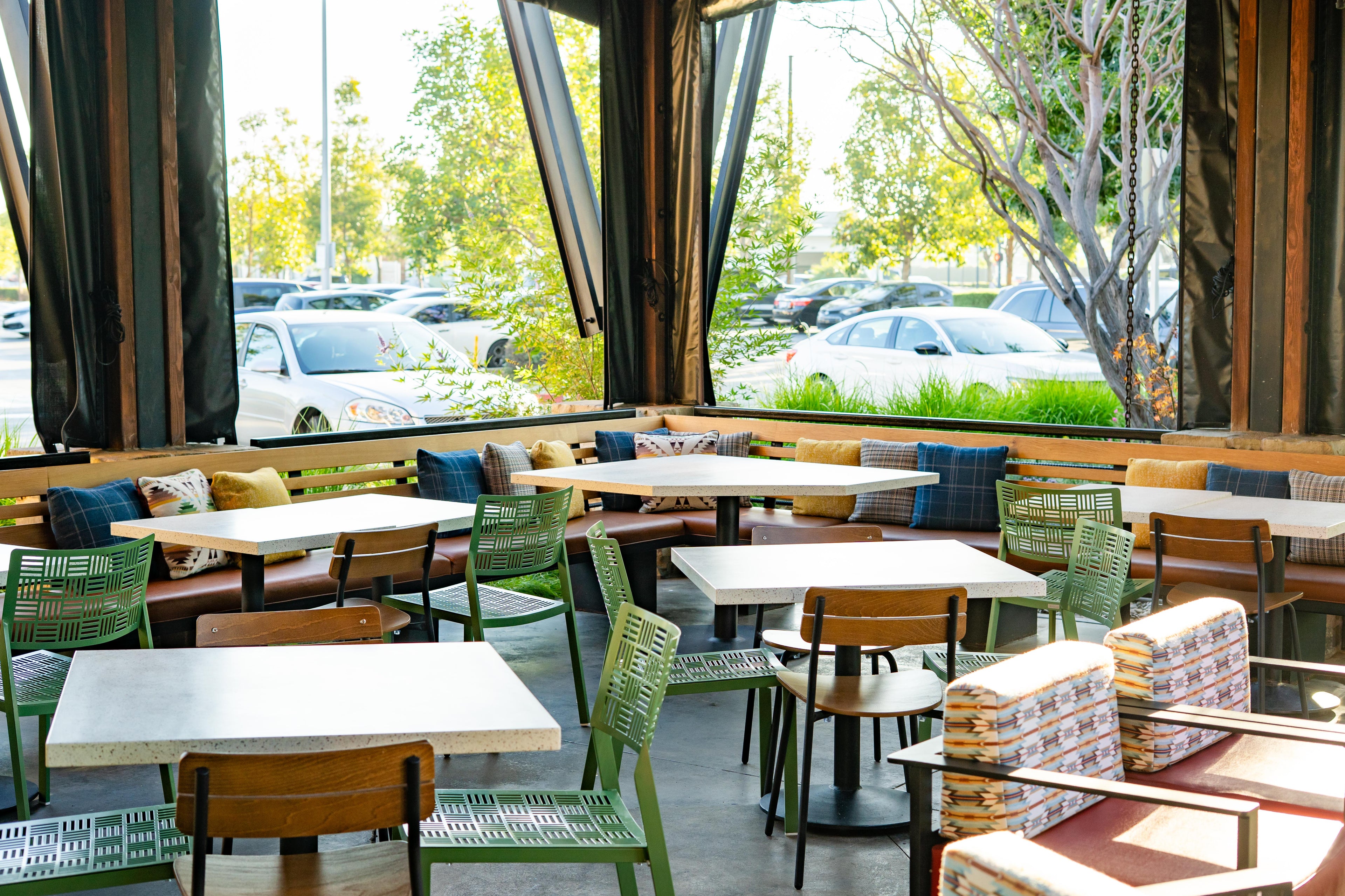Modern restaurant interior with tables, chairs, and large windows overlooking a parking lot.
